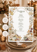 A white menu card with a decorative border of fall foliage, gourds, and fruit, with the text "Friendsgiving Menu" at the top, placed on a white plate with a gold rim on a table with fall decor.