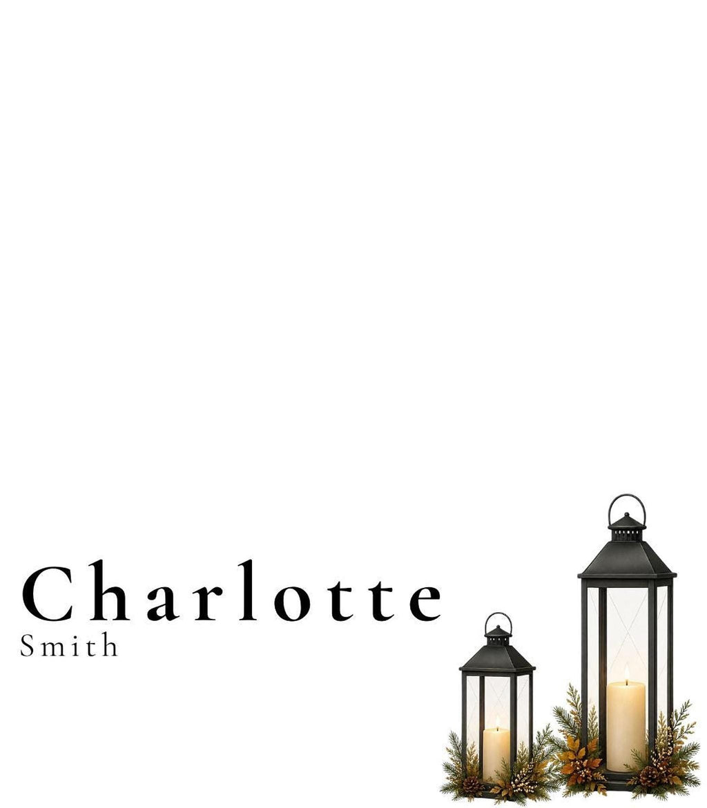 A white place card with the name "Charlotte Smith" in black text, with two black lanterns with candles and green and brown foliage at the bottom right.
