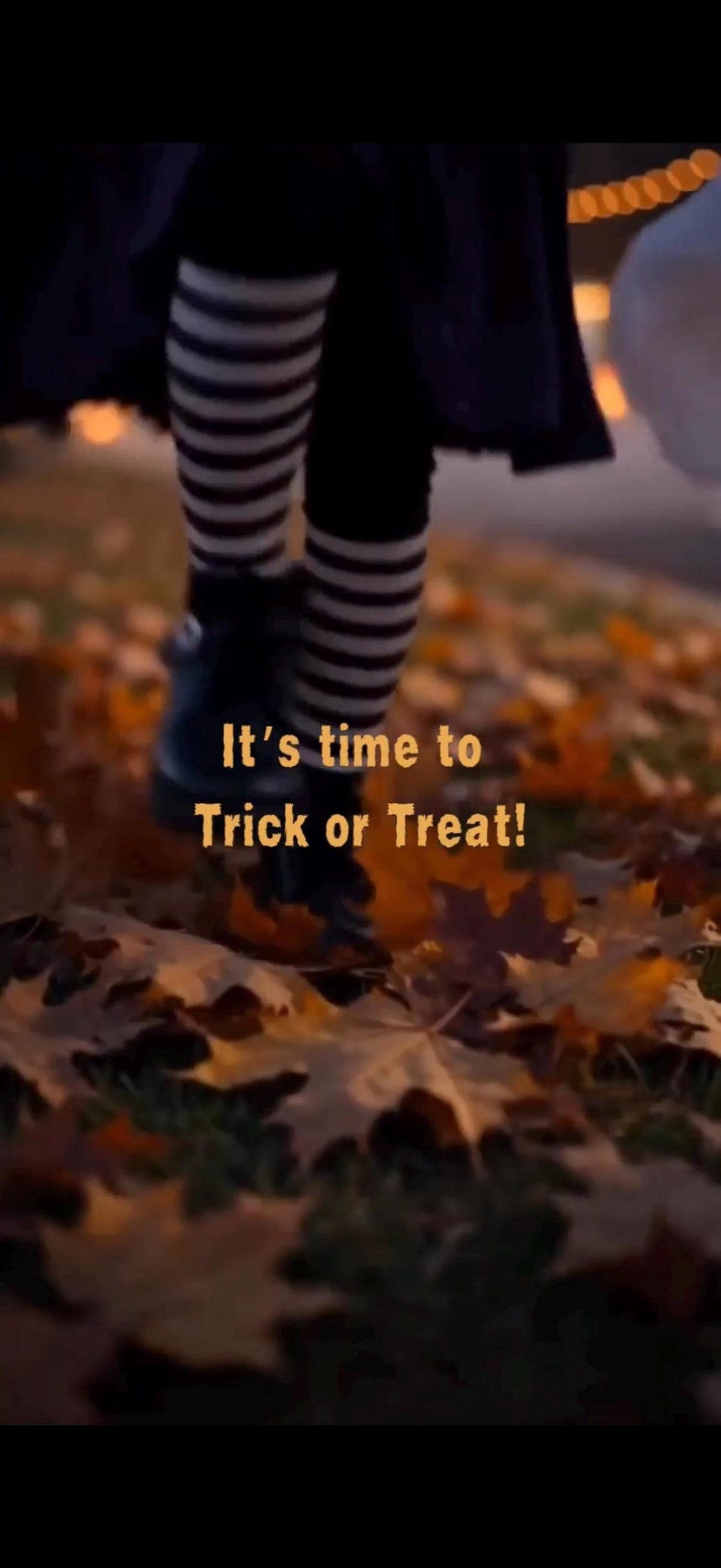 A person wearing black and white striped stockings and black shoes walks on a path covered with autumn leaves, with text "It's time to Trick or Treat!" superimposed.